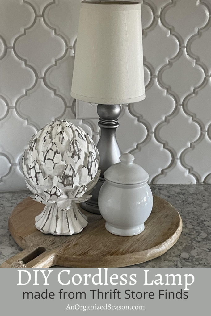Cordless lamp on a cutting board next to an artichoke statue and a white lidded bowl.  