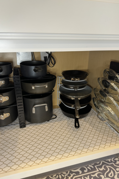 Pots, pans, and lids organized on racks in a kitchen cabinet.