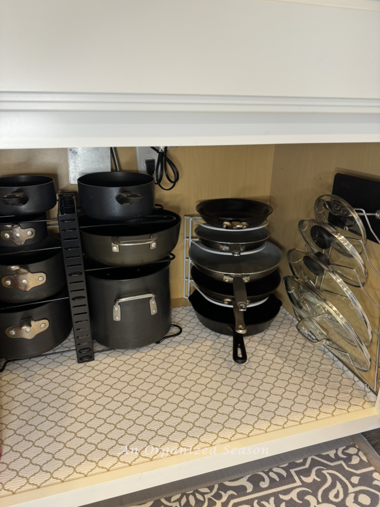 Cookware organized inside a kitchen cabinet with wire racks. 