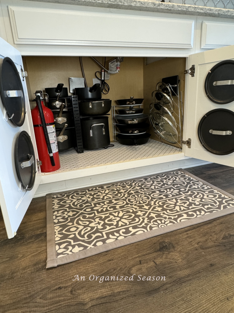 A kitchen cabinet with organized pots, pans, and lids. 