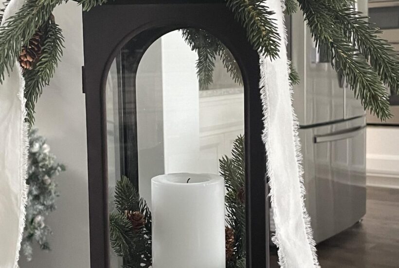 Lantern decorated with greenery, pinecones, and a white velvet ribbon.