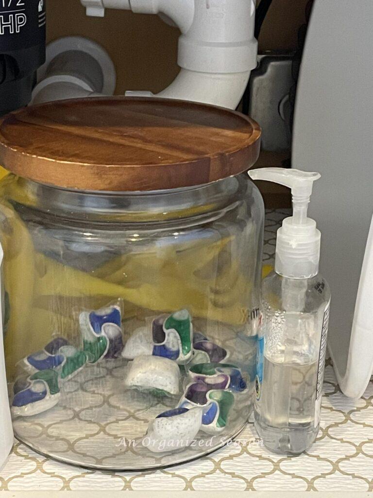 Glass jar with wood lid holding dishwasher pods. 