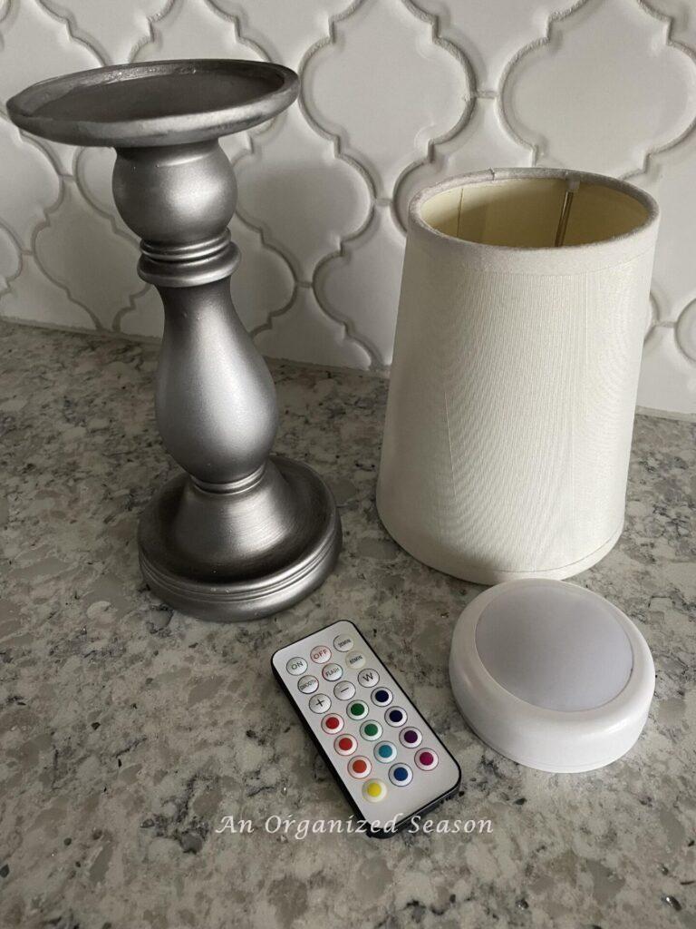 Step one to make a DIY lamp is to gather a candlestick, a mini lampshade, and a puck light with remote control. 