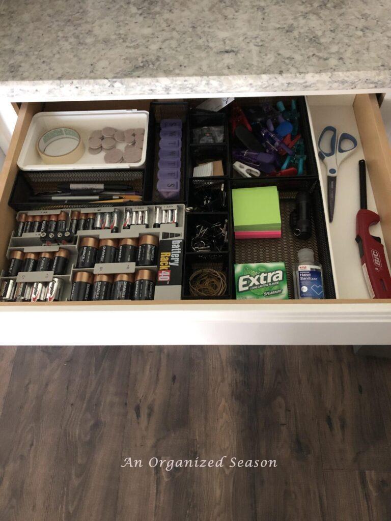 A junk drawer organized with black bins and a battery organizer. 