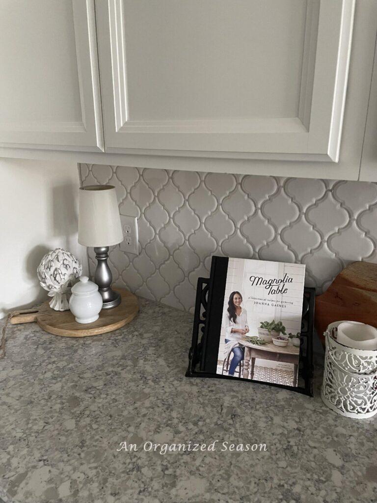 A kitchen counter decorated with a cookbook, cutting boards, a cordless lamp, and decorative items. 