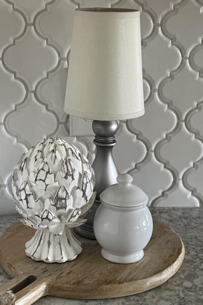 A cordless lamp, artichoke statue, and white bowl sitting on a cutting board.