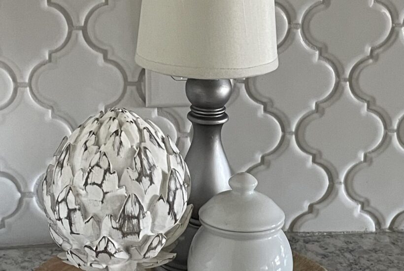 A cordless lamp, artichoke statue, and white bowl sitting on a cutting board.