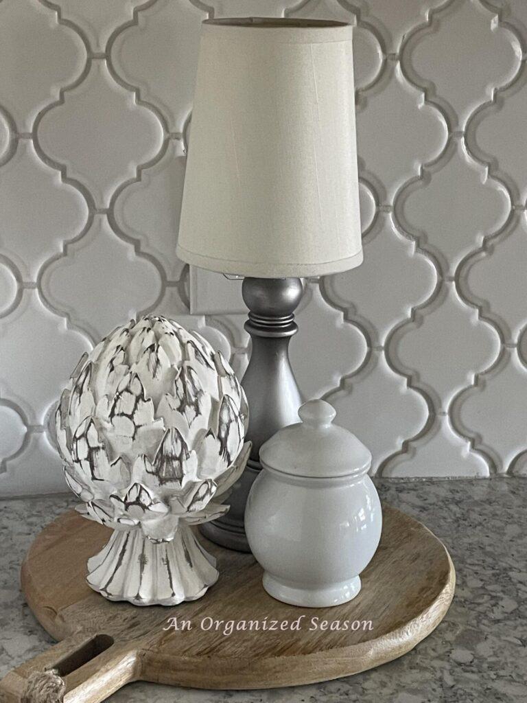 A cordless lamp, artichoke statue, and white bowl on a cutting board. 