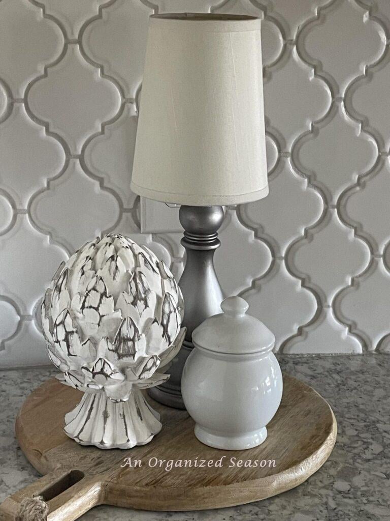 A cordless lamp, artichoke statue, and white bowl on a cutting board.