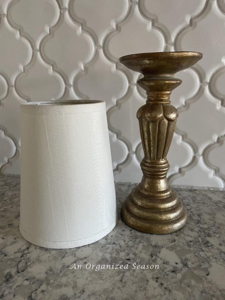 A white mini lampshade next to a gold candlestick.