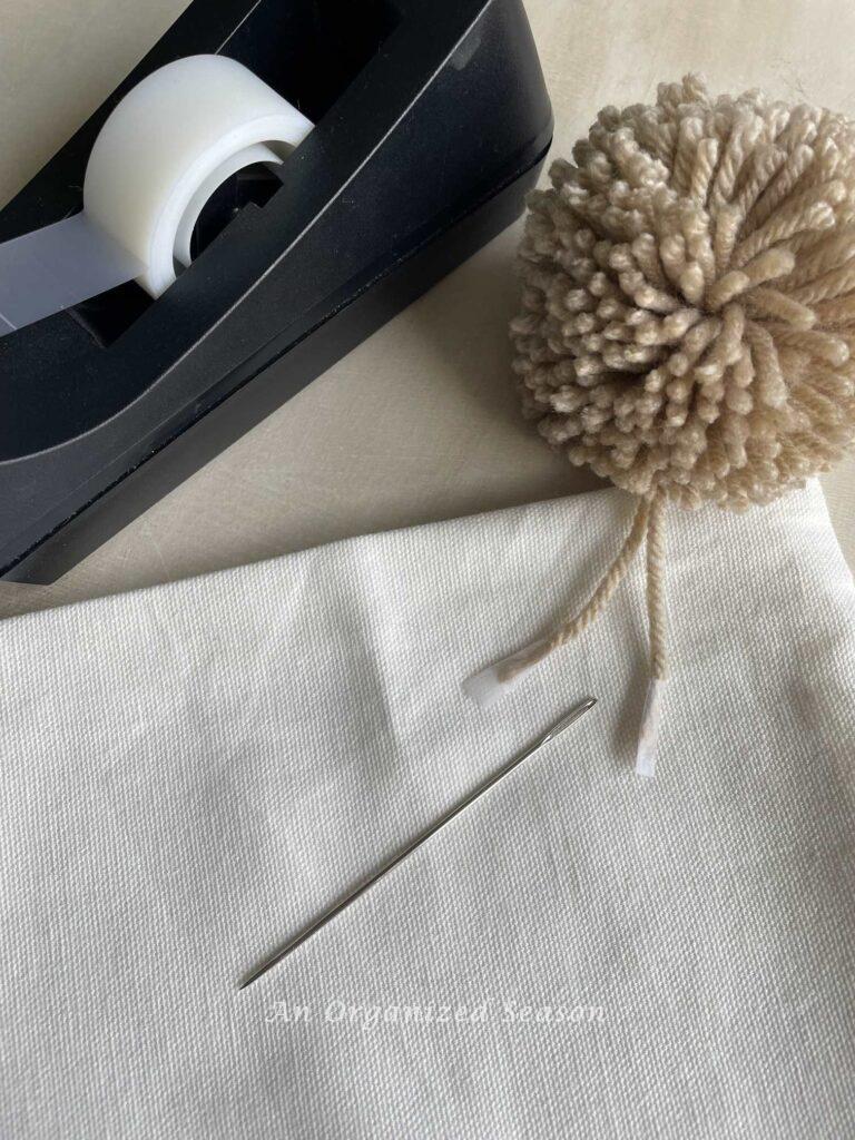 Make a DIY pillow by using a doll needle to attach a pom pom to a pillow cover. 