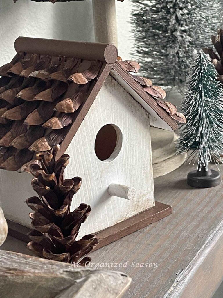 A white birdhouse with pinecone pieces on the roof. 