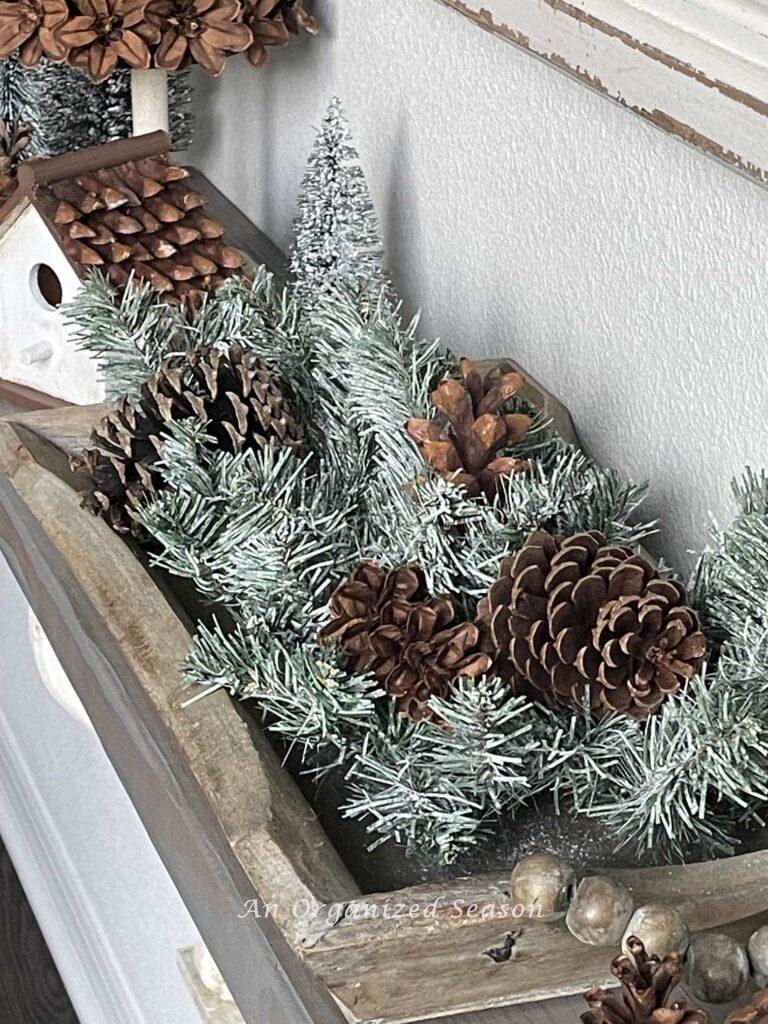 A wood tray filled with evergreen and pinecones. 