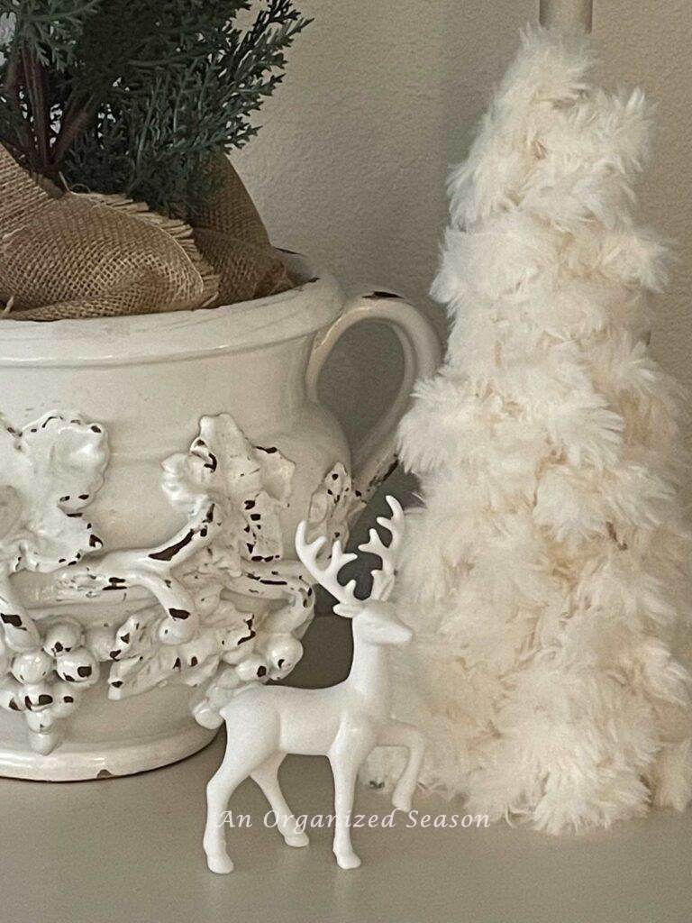 A white vase, yarn Christmas tree, and a white deer. 