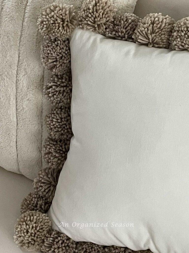 A pillow that has pom poms around the edge. 