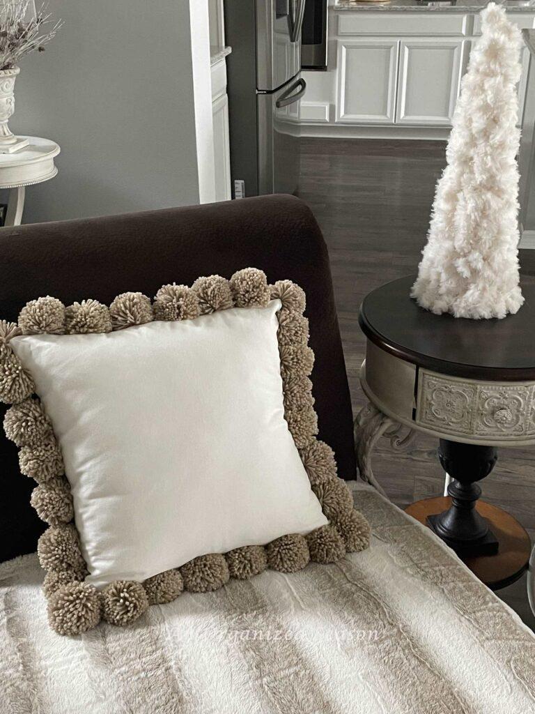 A pom pom pillow on a chaise lounge. 