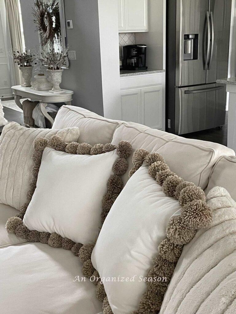 Two faux fir pillows and two pom pom pillows on a couch. 