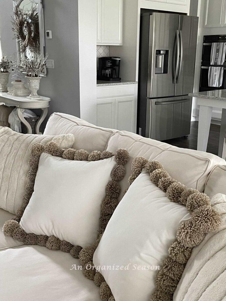 Two faux fur pillows next to two pom-pom pillows on a couch. 