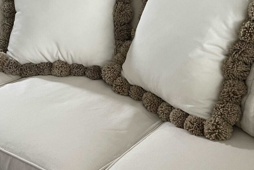 Two DIY pom pom pillows on a couch