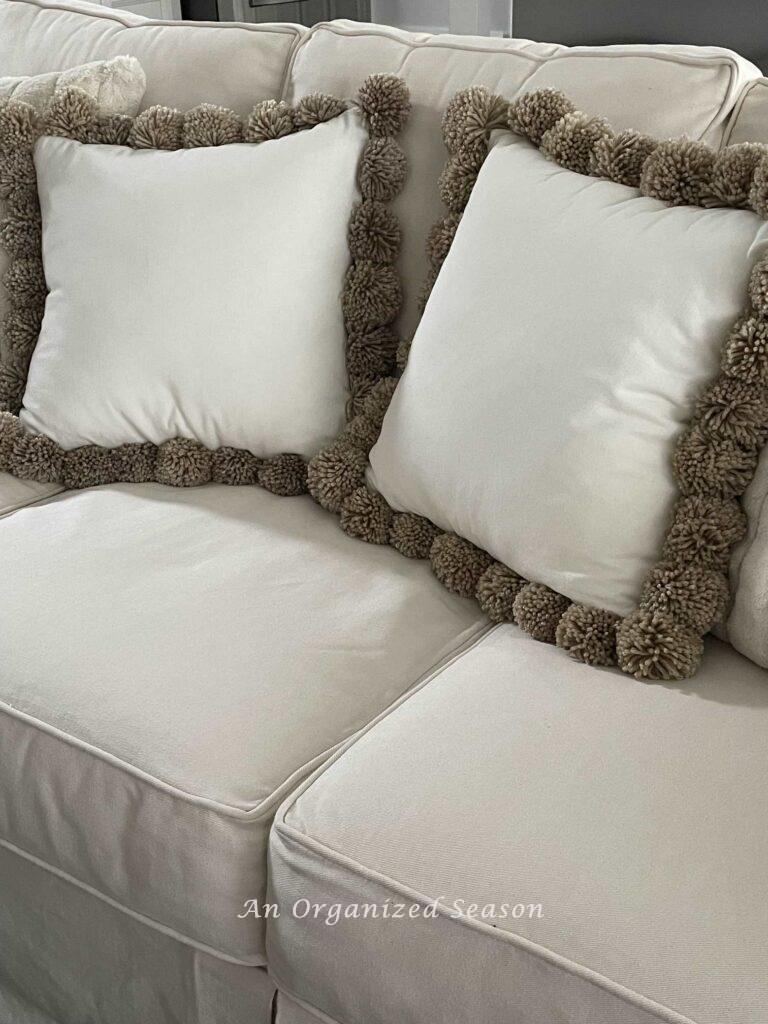 Two DIY pom pom pillows on a couch. 