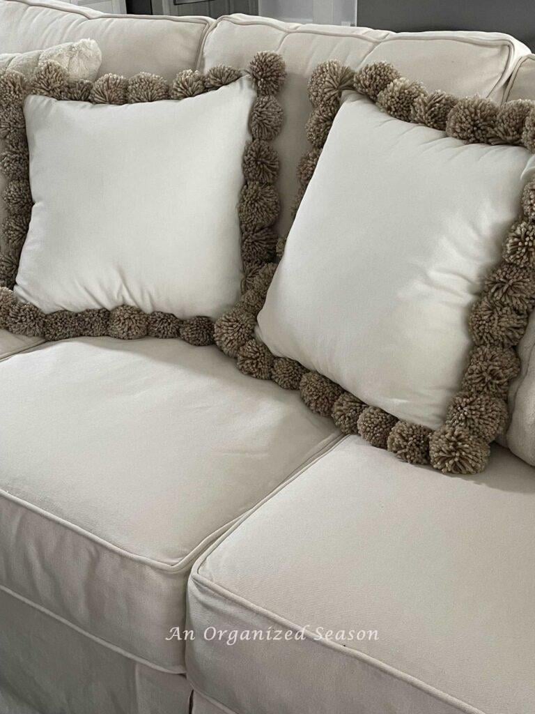 Two DIY pom pom pillows on a couch.