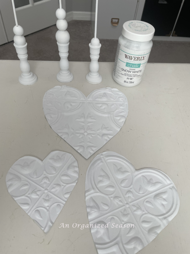 Three white hearts, white paint, and three wood stands used to make DIY Valentines decor.