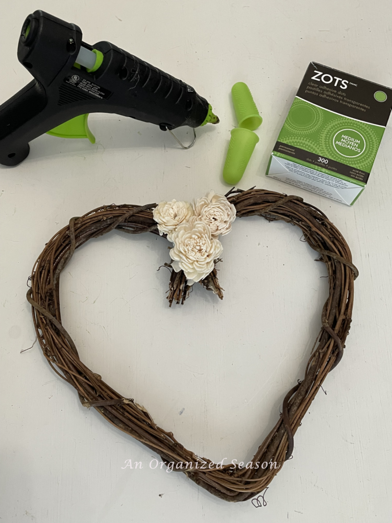 Step three to make a grapevine heart wreath DIY is to adhere the flowers to the wreath. 