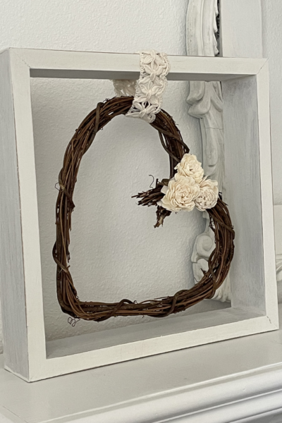 grapevine heart wreath hanging in square wood frame.