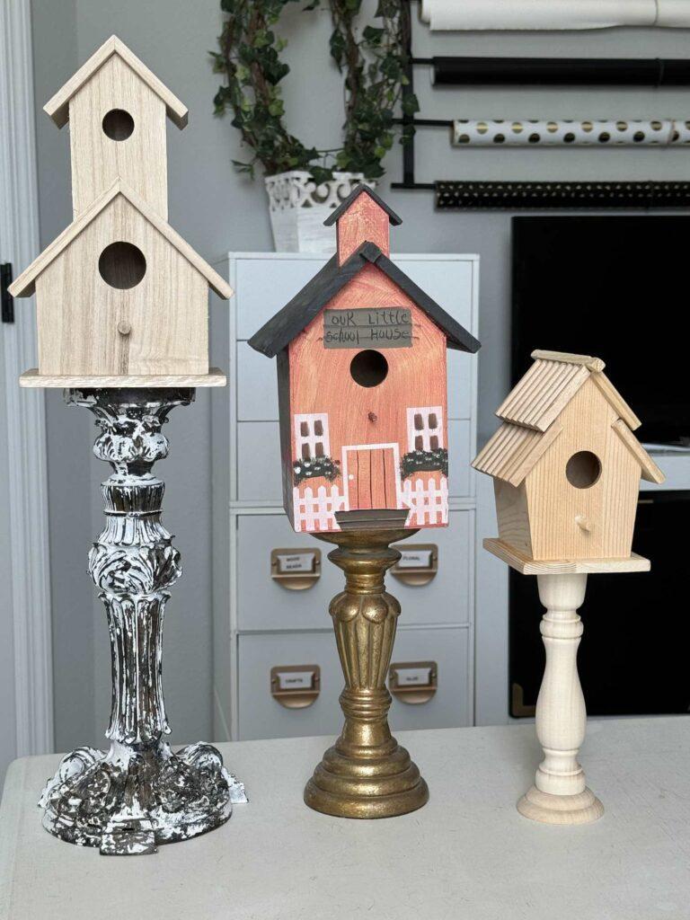 Birdhouses sitting on candlesticks that don't match. 