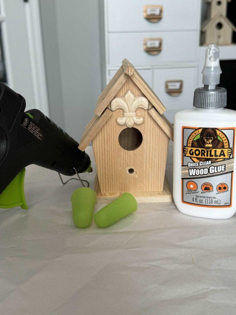 Wood birdhouse, wood glue, a glue gun, and finger protectors. 