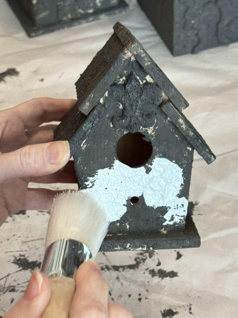 Someone painting a black birdhouse with white paint.