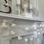 A pom pom garland and a heart garland hanging on a mantel.