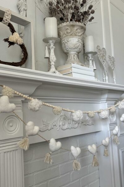 A pom pom garland and a heart garland hanging on a mantel.