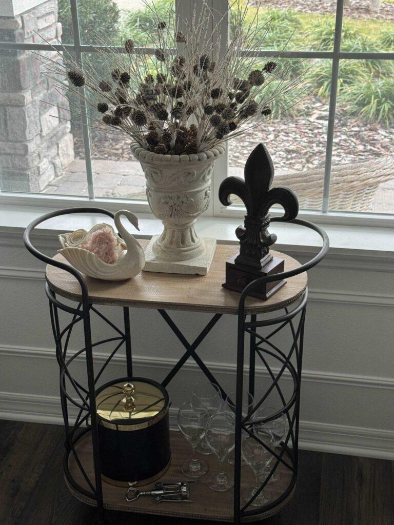 A bar cart decorated with a swan and a fleur dis li statue. 