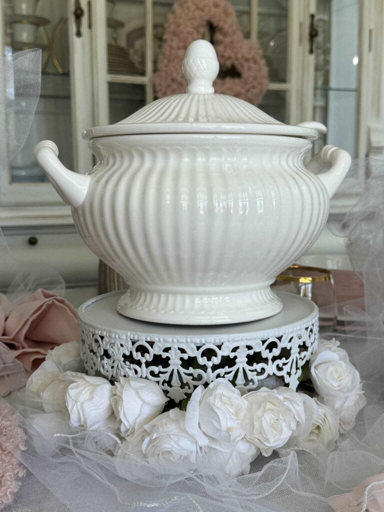 A white soup tureen on a cake stand surrounded by white roses makes pretty Valentine's table decor.  