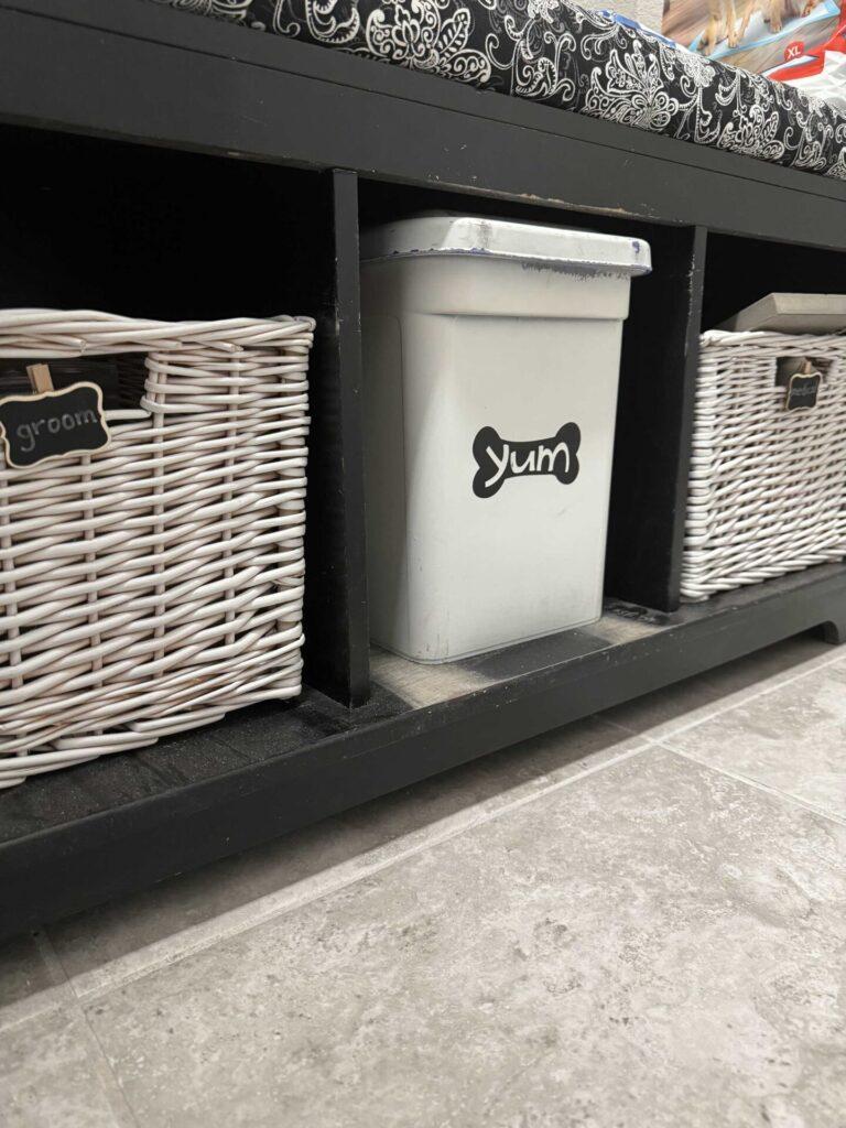 A black bench with two white baskets and a container of dog food. 