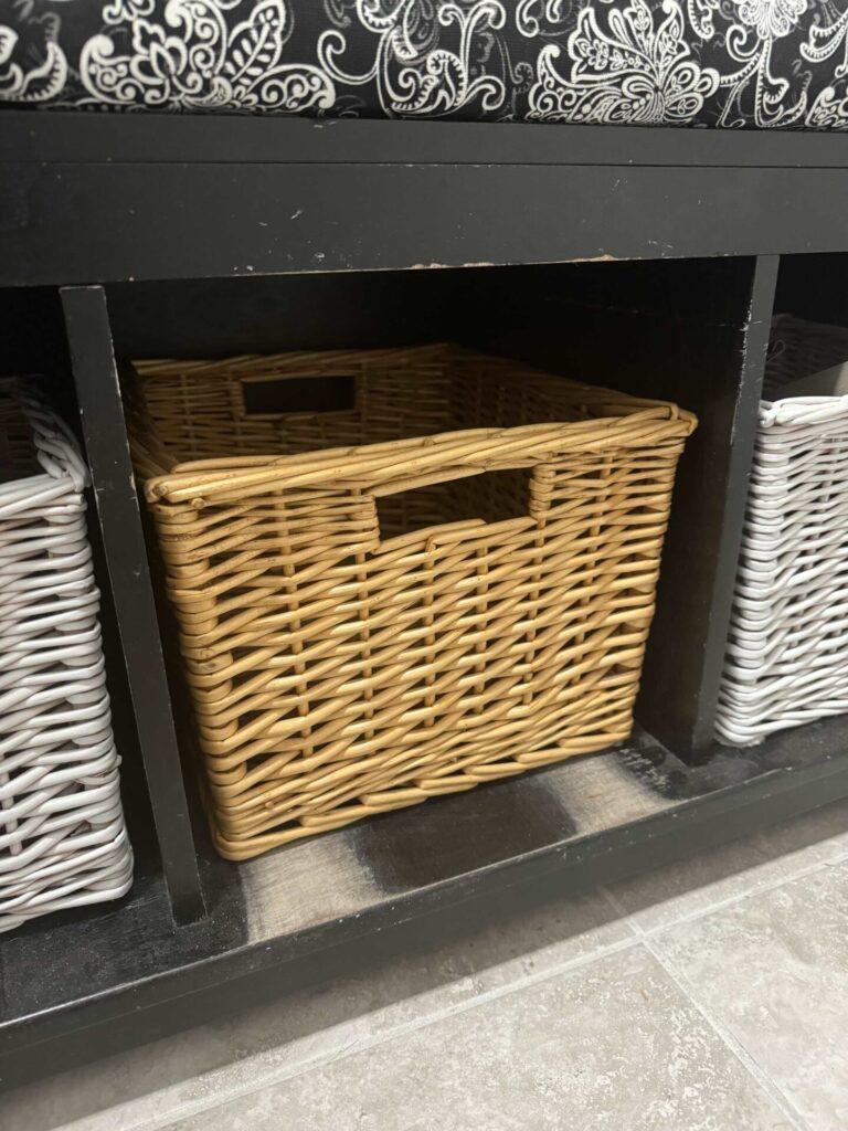 A tan basket in a black storage bench. 