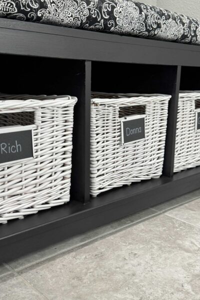 A black storage bench with white baskets and name labels.