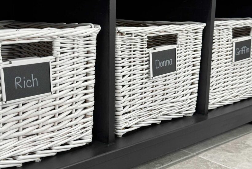 A black storage bench with white baskets and name labels.
