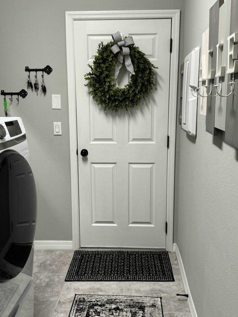 White entry door in a laundry room with a boxwood wreath and black and white stripped bow. 