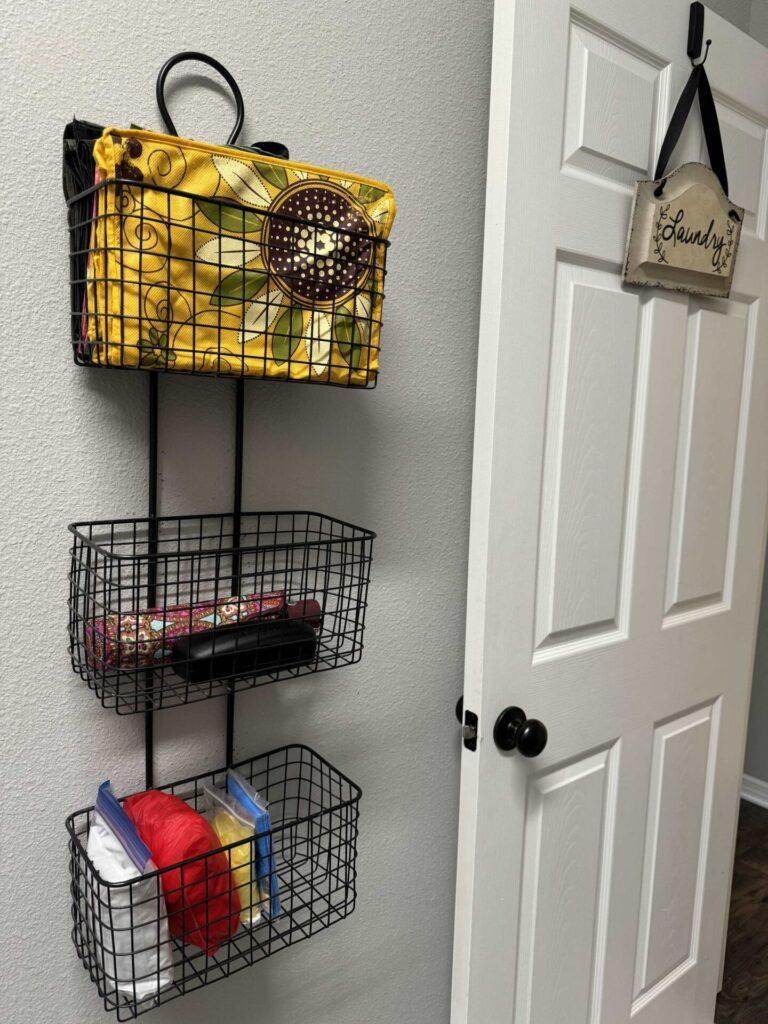 A three-tiered wire basket storing ponchos, umbrellas, sunglasses, and reusable grocery bags. 