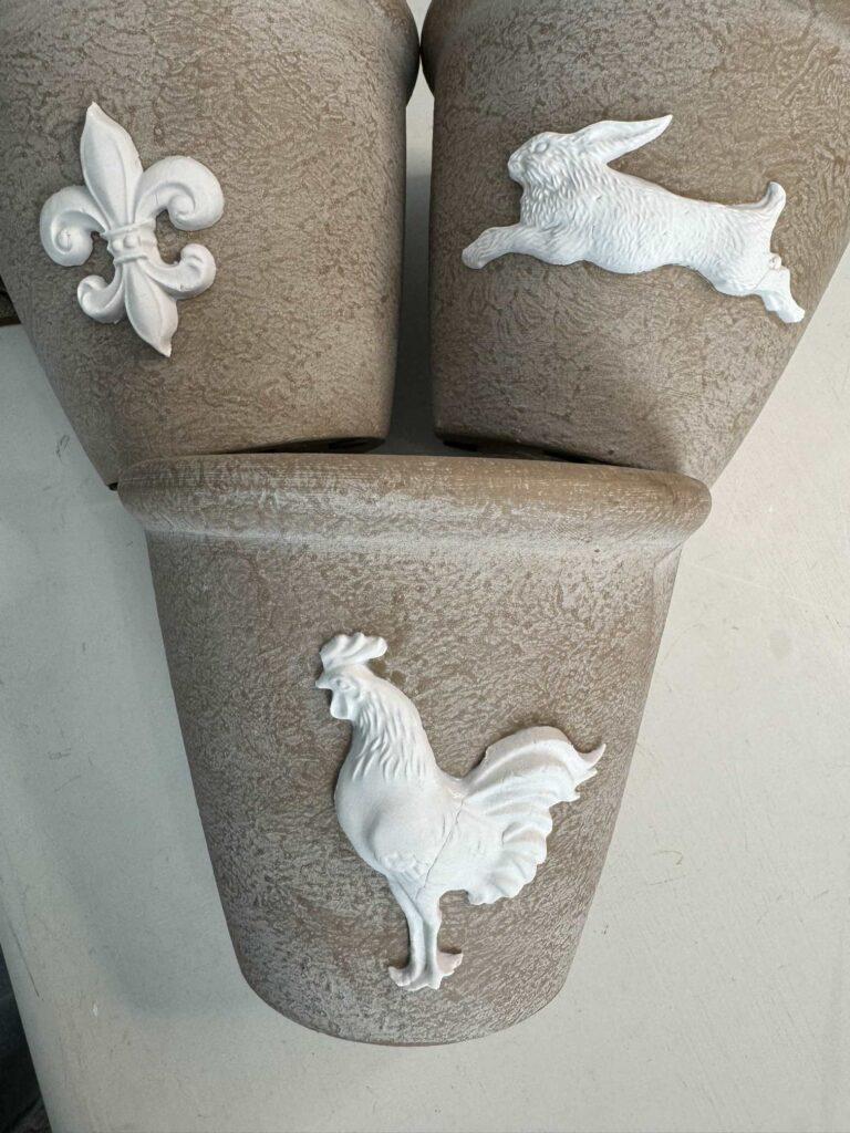 Three flower pots with air dry clay molds adhered to the front of them. 