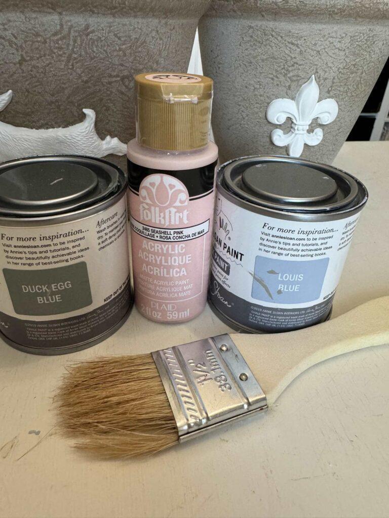 Three colors of paint and a chip brush used to make DIY flower pots.