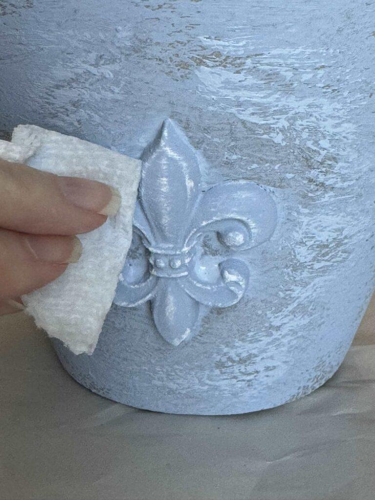 Someone wiping blue paint off of a fleur de lis casting. 