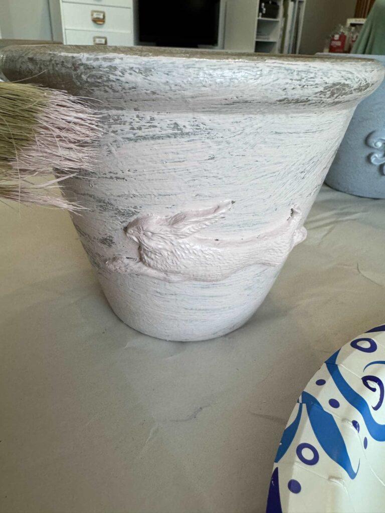 Someone brushing pink paint onto a pot. 