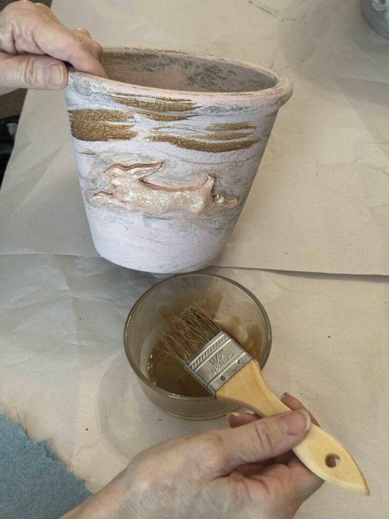 Someone painting a brown wash onto a flower pot. 