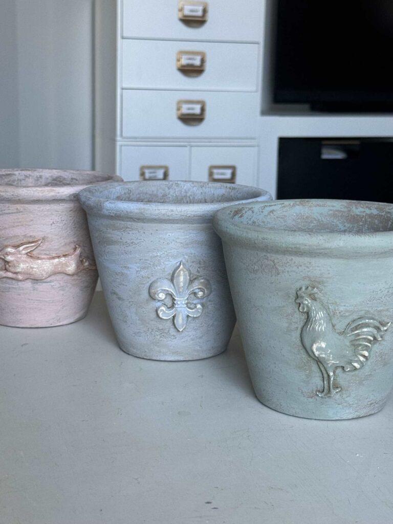 Three DIY flower pots embellished with clay molds, painted, and aged. 