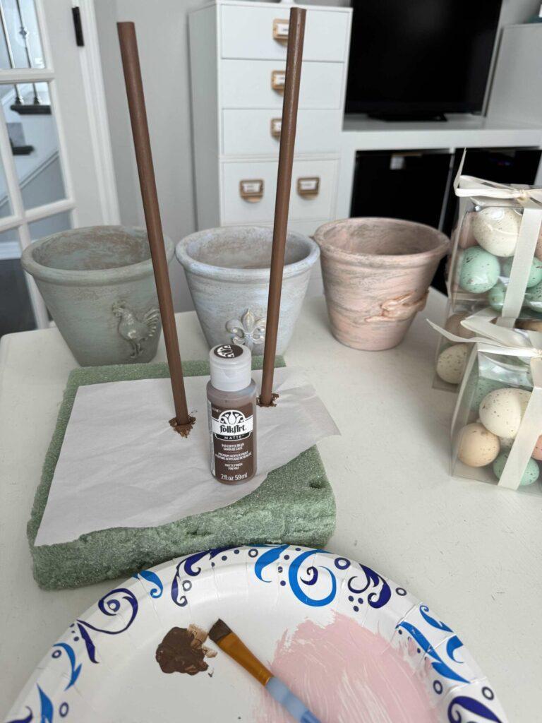 Step one to make an Easter egg topiary is to paint dowel rods brown. 