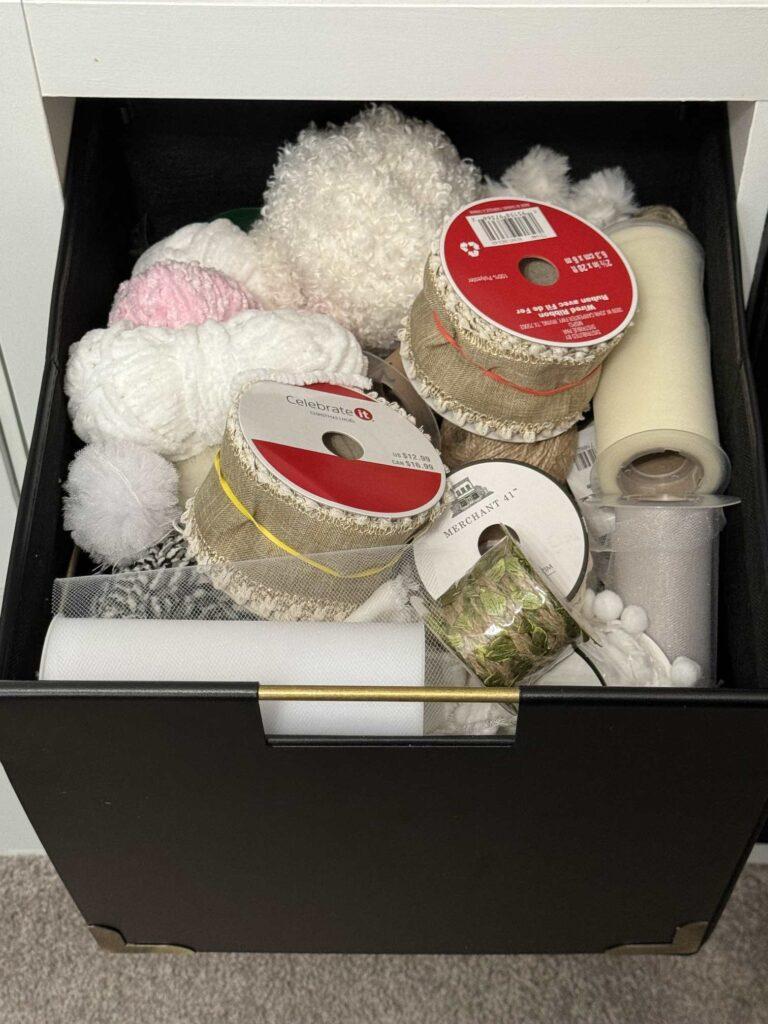 A black storage cube filled with yarn and ribbon. 