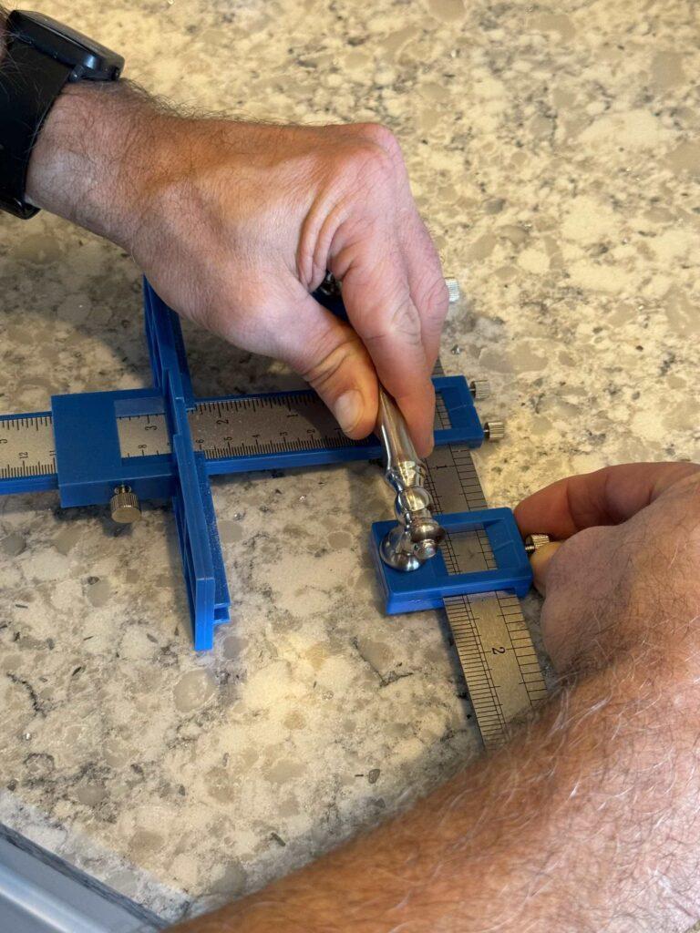 A silver cabinet pull being held on a jig. 